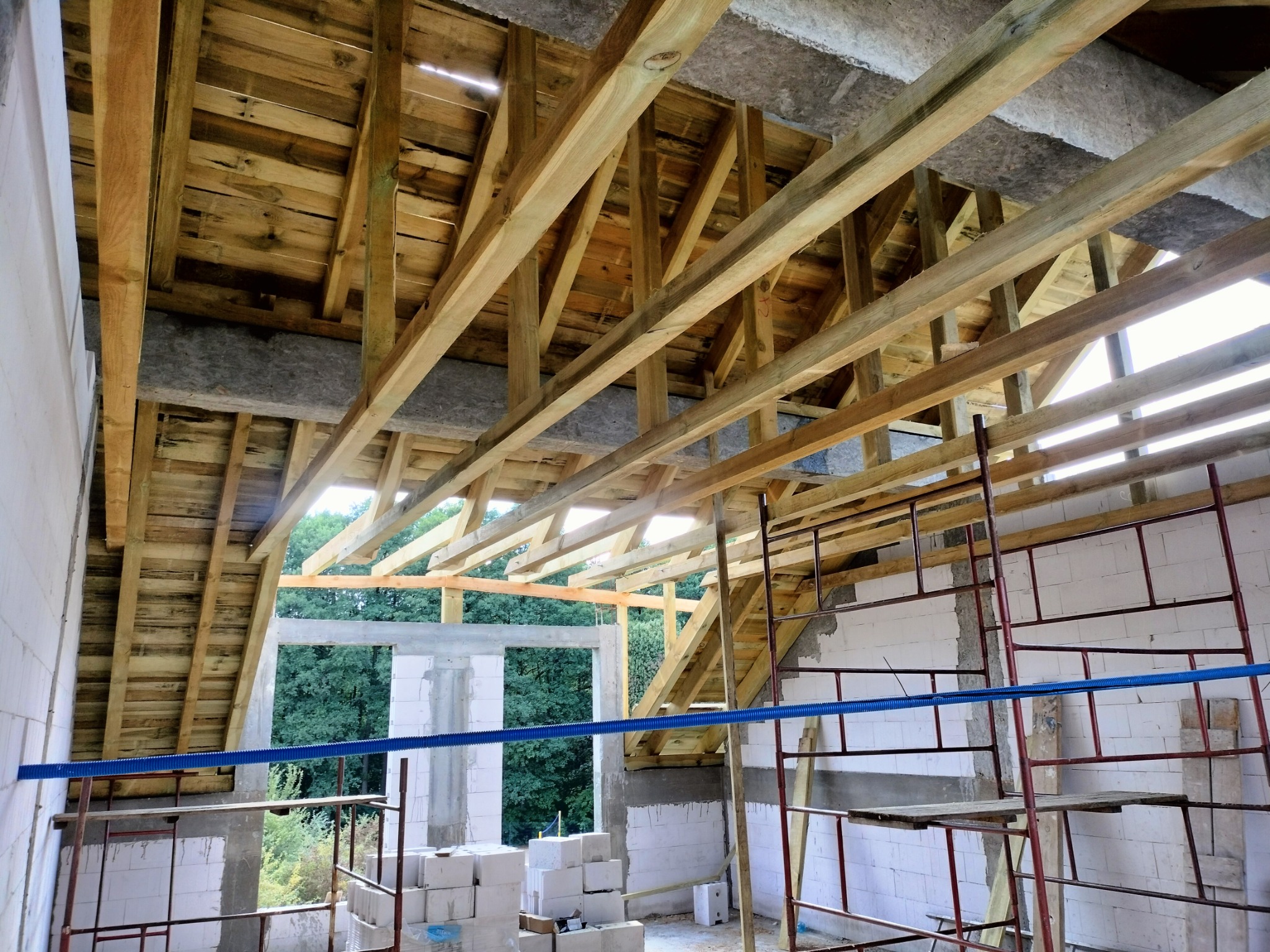 Wnętrze budynku w trakcie budowy dachu z widoczną drewnianą więźbą dachową, izolacją i rusztowaniem.