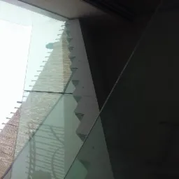 Szklana ściana budynku z widocznymi mocowaniami i elementami konstrukcyjnymi, ujęcie z dołu pod kątem w pochmurny dzień.