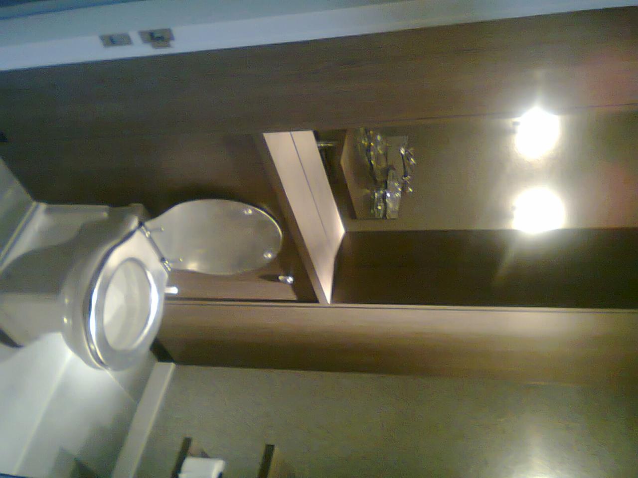 Nowoczesna toaleta podwieszana z otwartą klapą, widok z dołu, oświetlenie punktowe, ciemne drewniane wykończenie ściany.