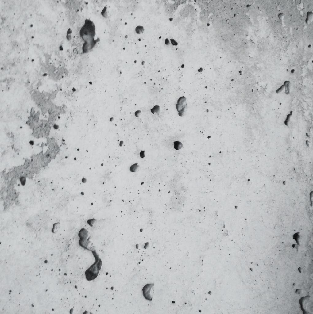 Szara, porowata powierzchnia betonu z widocznymi wżerami i nierównościami, ukazująca surową teksturę materiału.