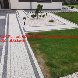 Ułożona nawierzchnia z kostki w dwóch odcieniach szarości, tworząca ścieżkę i obramowanie rabaty z białym żwirem, z widocznym trawnikiem i elementami małej architektury ogrodowej