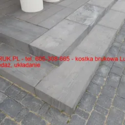 Schody wyłożone szarą kostką betonową imitującą drewno, z widoczną fakturą słoj&oacute;w, obok ułożona kostka brukowa w kolorze szarym, ułożona w regularny wz&oacute;r.