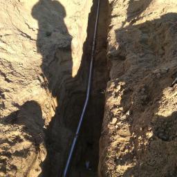 SPAWINSTAL - Rów z ułożoną rurą, cień osoby widoczny na skarpie wykopu.