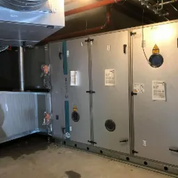 Rozbudowana instalacja wentylacyjna Systemair w pomieszczeniu technicznym, widoczne elementy kanałów i modułowa centrala wentylacyjna z dokumentacją techniczną na obudowie.