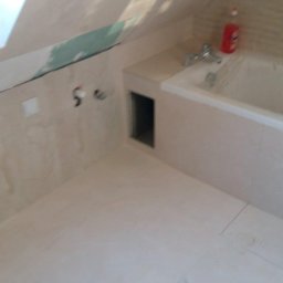 Pat-Bud - Wykończona łazienka na poddaszu z beżowymi płytkami, wanną i małym otworem rewizyjnym. Widoczne fragmenty niedokończonych prac na ścianie.