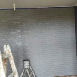 Pat-Bud - Ściana z efektem cegły pomalowana na szaro, drabina malarska i puszka farby. Widoczne ślady po taśmie malarskiej na suficie.