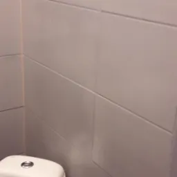 Toaleta z białą ceramiką i szare płytki ścienne ułożone poziomo w łazience.