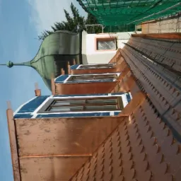 Miedziany dach z lukarnami i wieżyczką w trakcie prac wykończeniowych, widoczna membrana i rusztowania zabezpieczające.