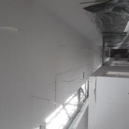 Remonter - Wnętrze w trakcie prac wykończeniowych: świeżo pomalowana ściana i sufit na biało, widoczne kable wystające ze ściany oraz zabezpieczona folią część sufitu.