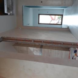 Remonter - Wnętrze w trakcie prac wykończeniowych, widoczne ściany po nałożeniu gładzi, przygotowane do dalszego etapu, z widocznymi otworami okiennymi i elementami instalacji.