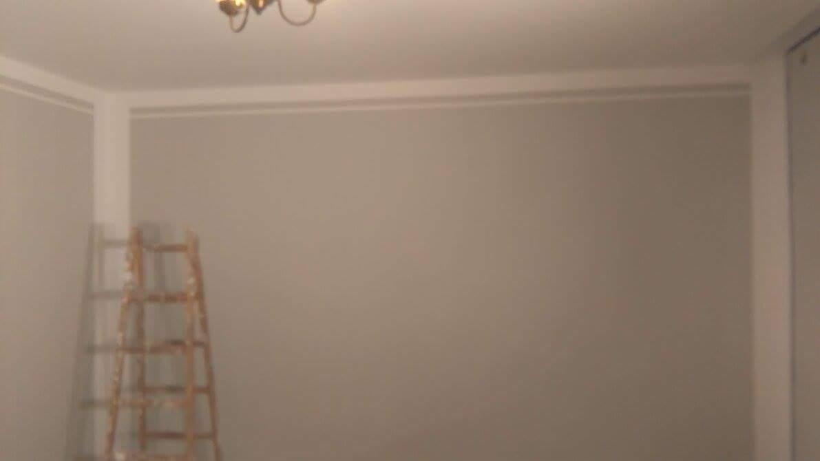 Świeżo pomalowane, jednolite ściany w odcieniach szarości z drewnianą drabiną opartą o ścianę, widoczny fragment sufitu z lampą.