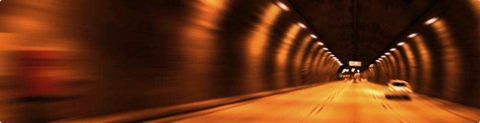 Rozmazane zdjęcie wnętrza tunelu samochodowego z widocznymi światłami i samochodem w oddali, efekt rozmycia dynamicznego.