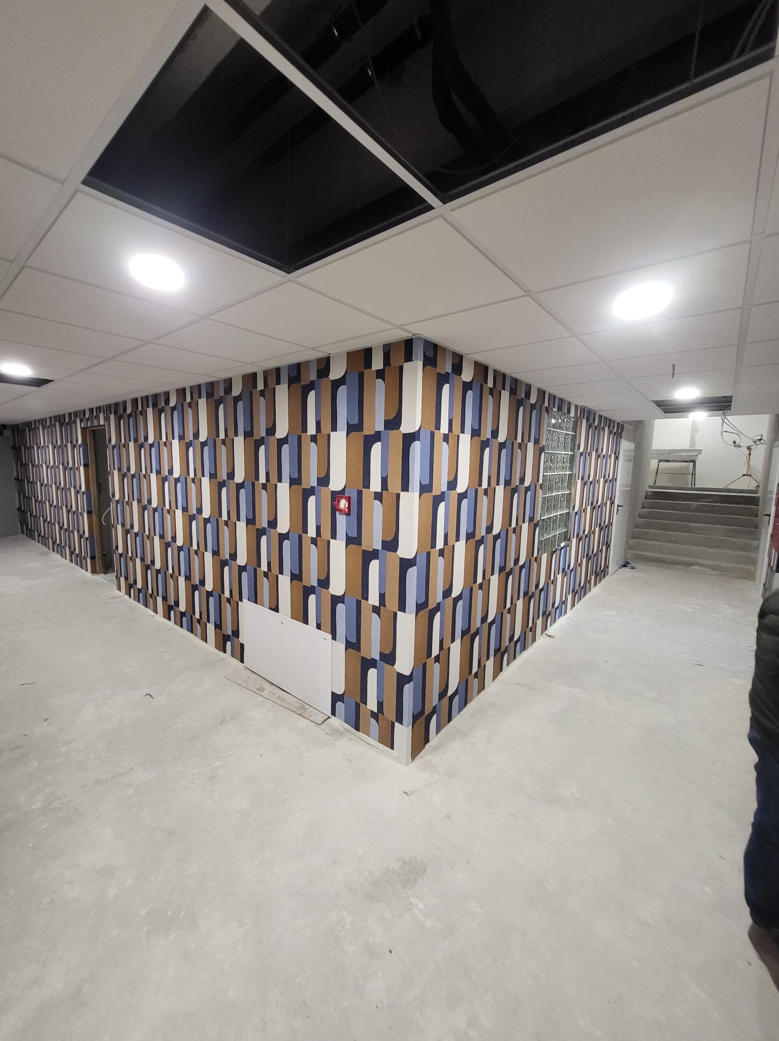 Korytarz z nową tapetą w geometryczne wzory w odcieniach brązu i błękitu, wykończony sufit z panelami i oświetleniem punktowym, w trakcie remontu.