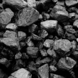 Góra brył węgla o nieregularnych kształtach, oświetlona z góry, z widoczną strukturą i matową powierzchnią.