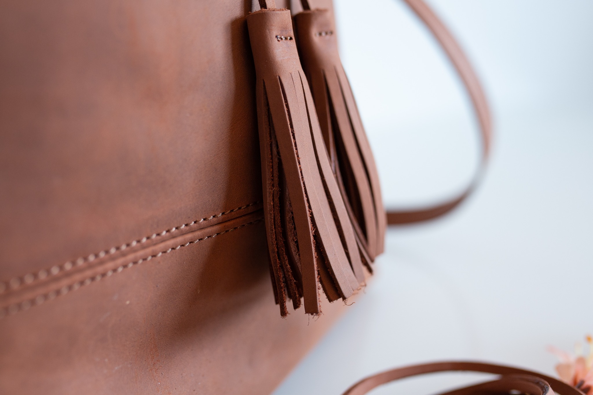 Brązowa skórzana torebka z frędzlami, widoczny detal szwu i paska na jasnym tle.