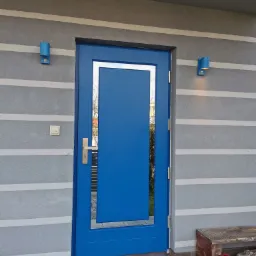 Niebieskie drzwi zewnętrzne z srebrną ramką, zamontowane w szarej ścianie z poziomymi pasami, oświetlone przez dwie niebieskie lampy ścienne.