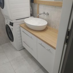 ROBERT DAWID - Nowoczesna łazienka z umywalką nablatową na szafce z drewnianym blatem, pralka i suszarka ustawione jedna na drugiej, szare płytki i minimalistyczna armatura.