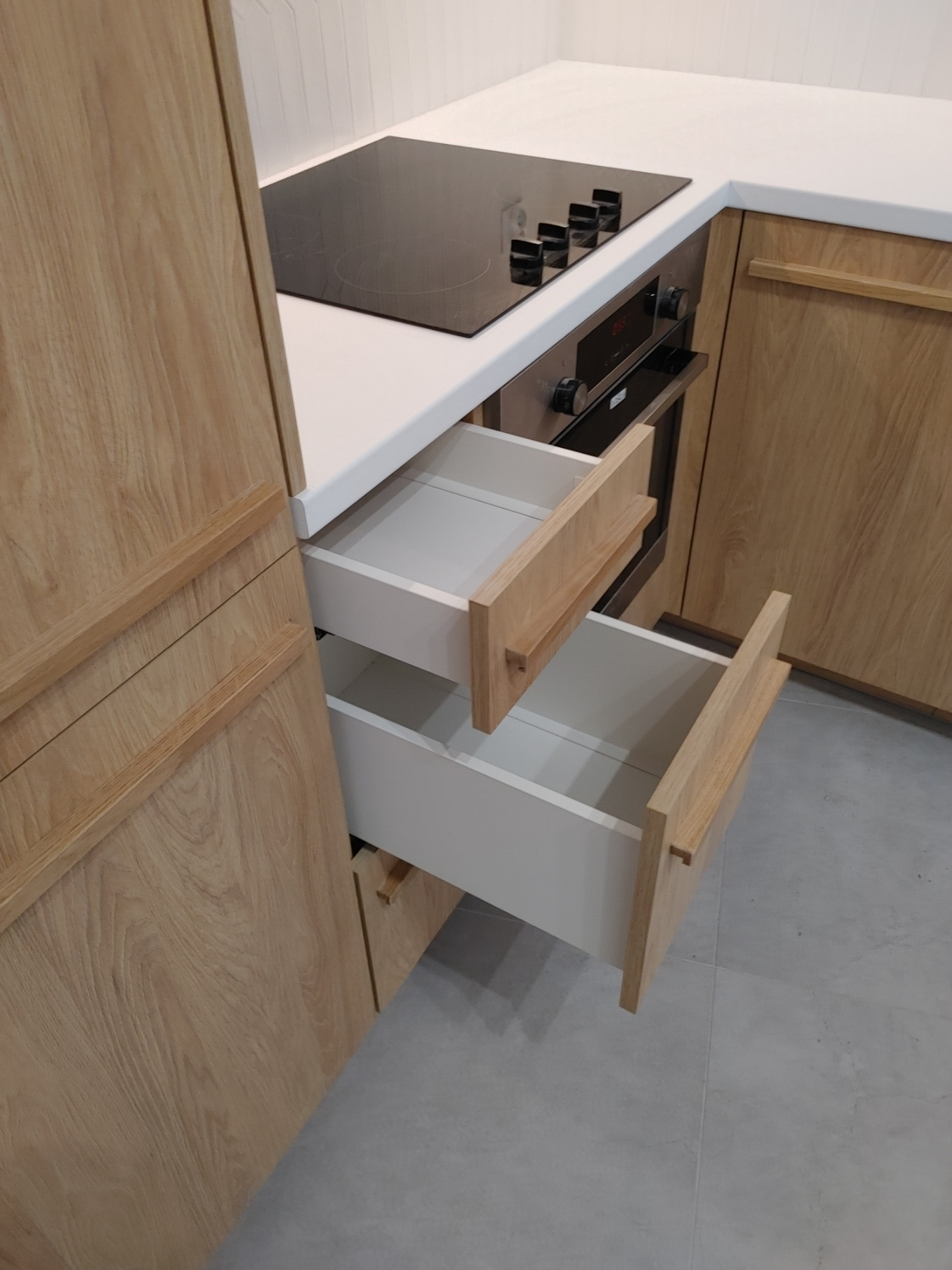 Otwarta szuflada z drewnianymi uchwytami w zabudowie kuchennej z blatem i płytą indukcyjną.