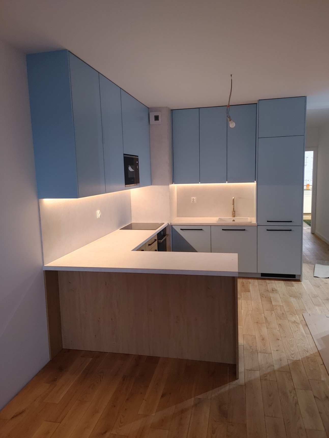 Nowoczesna kuchnia w odcieniach błękitu i drewna z podświetleniem LED, widok na wyspę kuchenną i część szafek wiszących.