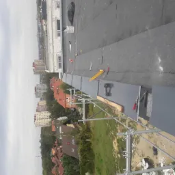 Fragment płaskiego dachu z papy w trakcie prac, widoczne narzędzia, rusztowanie i panorama miasta w tle.