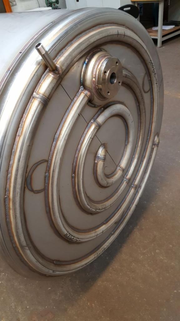 Zbliżenie na spawany element ze stali nierdzewnej z spiralnie ułożonymi rurami, zakończony kołnierzem, widoczne ślady po spawaniu i oznaczenia techniczne.