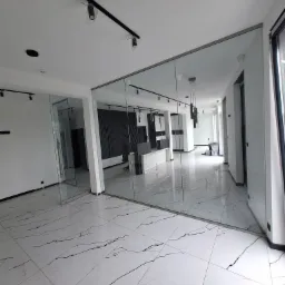 Nowoczesne biuro po remoncie: białe ściany, podłoga z białego marmuru z czarnymi żyłami, szklane ścianki działowe z metalowymi ramami, czarne reflektory sufitowe na szynoprzewodach.