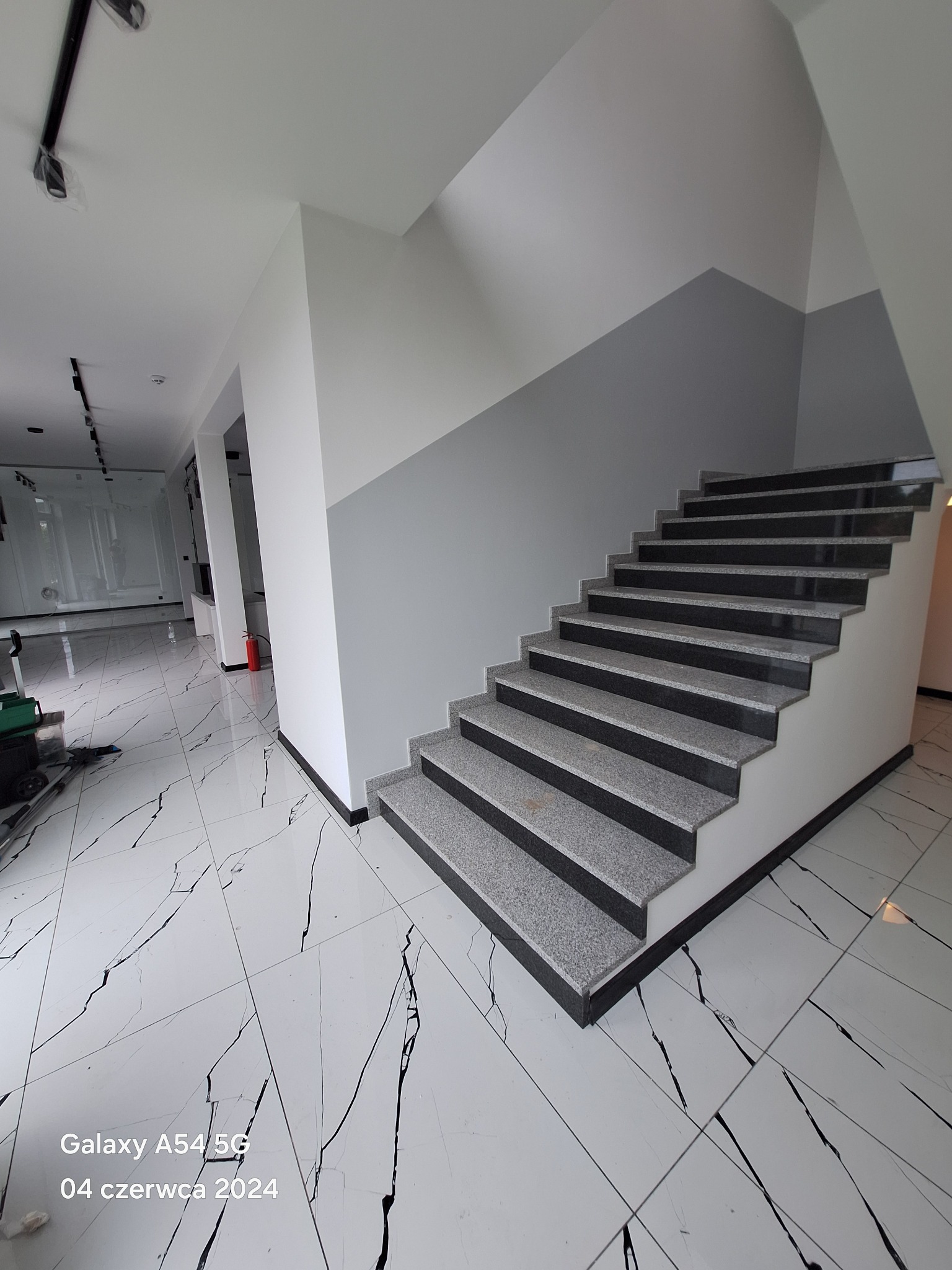 Wykończone schody z szarymi stopniami i czarnymi krawędziami w nowoczesnym wnętrzu z białymi ścianami i podłogą w czarne żyły.