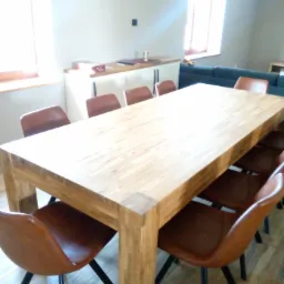 Jasny, prostokątny stół z litego drewna z ośmioma krzesłami z brązowej ekoskóry na czarnych, metalowych nogach w jasnym wnętrzu.