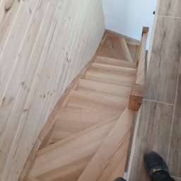 Drewutnia Mazurska Marcin Barczewski - Drewniane schody z jasnego drewna, widok z góry, stopnie z wyraźnym usłojeniem, drewniana boazeria na ścianie, fragment podłogi z płytek.