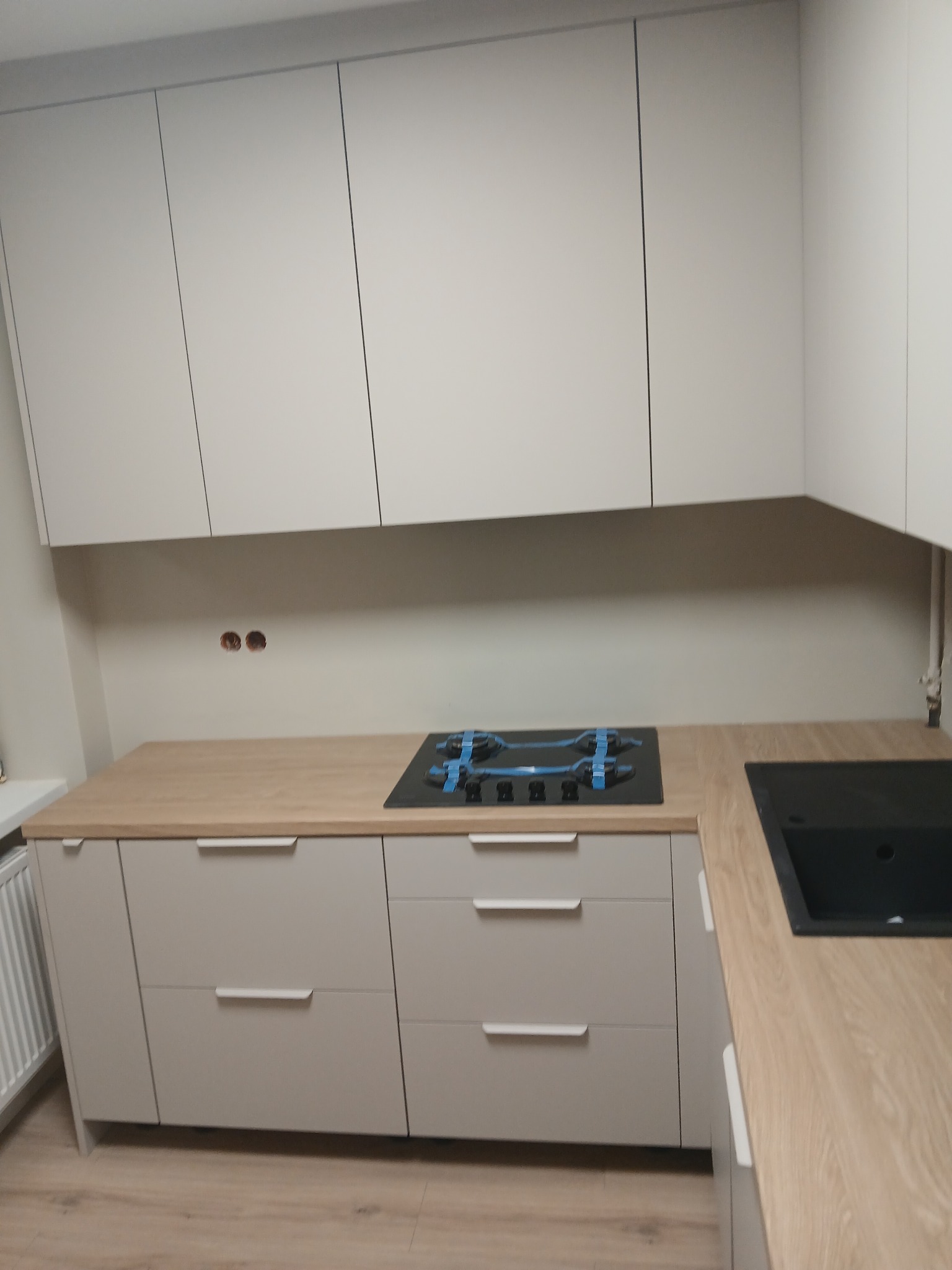 Jasna kuchnia na wymiar z drewnianym blatem i płytą gazową w Wieliczce. Minimalistyczny design, gładkie fronty szafek i szuflad, nowoczesne wykończenie.