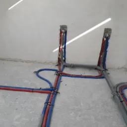 Wewnętrzne rozprowadzenie rur wodnych i kanalizacyjnych w surowym stanie, z widocznymi mocowaniami i pianką montażową przy ścianach.