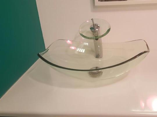 Szklana umywalka z baterią o szklanym dysku na blacie, widok z boku, na tle zielonej ściany i białej ściany z obrazem.