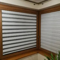 Kąt okienny z drewnianą ramą, wyposażony w rolety dzień noc w odcieniach szarości i bieli, z widoczną dekoracyjną zasłoną i rośliną doniczkową w tle.