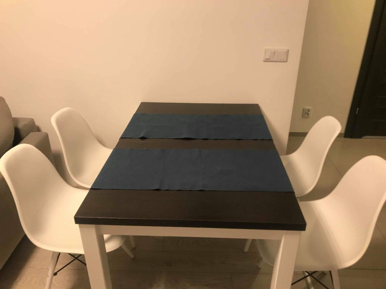 Stół z ciemnym blatem i białymi nogami, nakryty dwoma granatowymi bieżnikami, otoczony czterema białymi krzesłami w minimalistycznym stylu, na tle jasnej ściany.