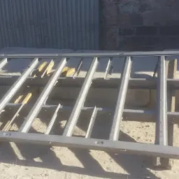 Metalowa konstrukcja ramowa z poprzeczkami, prawdopodobnie po obróbce, leżąca na ziemi w szarym odcieniu, z widocznymi śladami obróbki na spawach i powierzchni