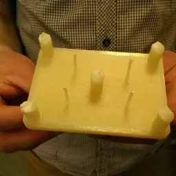 Żółty prototypowy model z tworzywa sztucznego z wystającymi elementami, trzymany w dłoniach na tle koszuli w kratę.