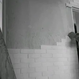 Montaż białej cegły dekoracyjnej na ścianie, widoczne ślady kleju i częściowo przygotowana powierzchnia, fragment drabiny po lewej stronie.