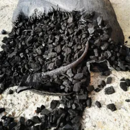 Wysypany ekogroszek z szarego, worka jutowego na betonowej powierzchni, widoczne fragmenty worka i drobne kawałki węgla rozrzucone wokół.