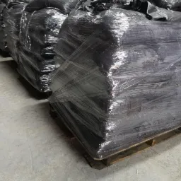 Rząd palet z workami, owiniętych folią stretch, składowanych w magazynie, widoczne szare betonowe podłoże.