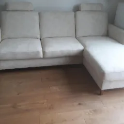 Jasny, narożny wypoczynek z zagłówkami, ustawiony na parkiecie w mieszkaniu.