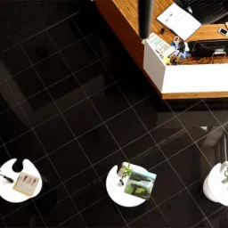 Błyszcząca, czarna podłoga z płytek w biurze, widok z góry, z recepcją i stolikami kawowymi z roślinami.