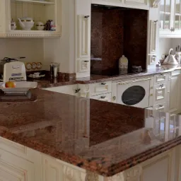Błyszczący, brązowo-czerwony blat w klasycznej kuchni z kremowymi szafkami i dekoracyjnymi detalami.