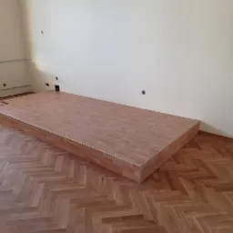 Podwyższenie z paneli podłogowych w pomieszczeniu z parkietem ułożonym w jodełkę.