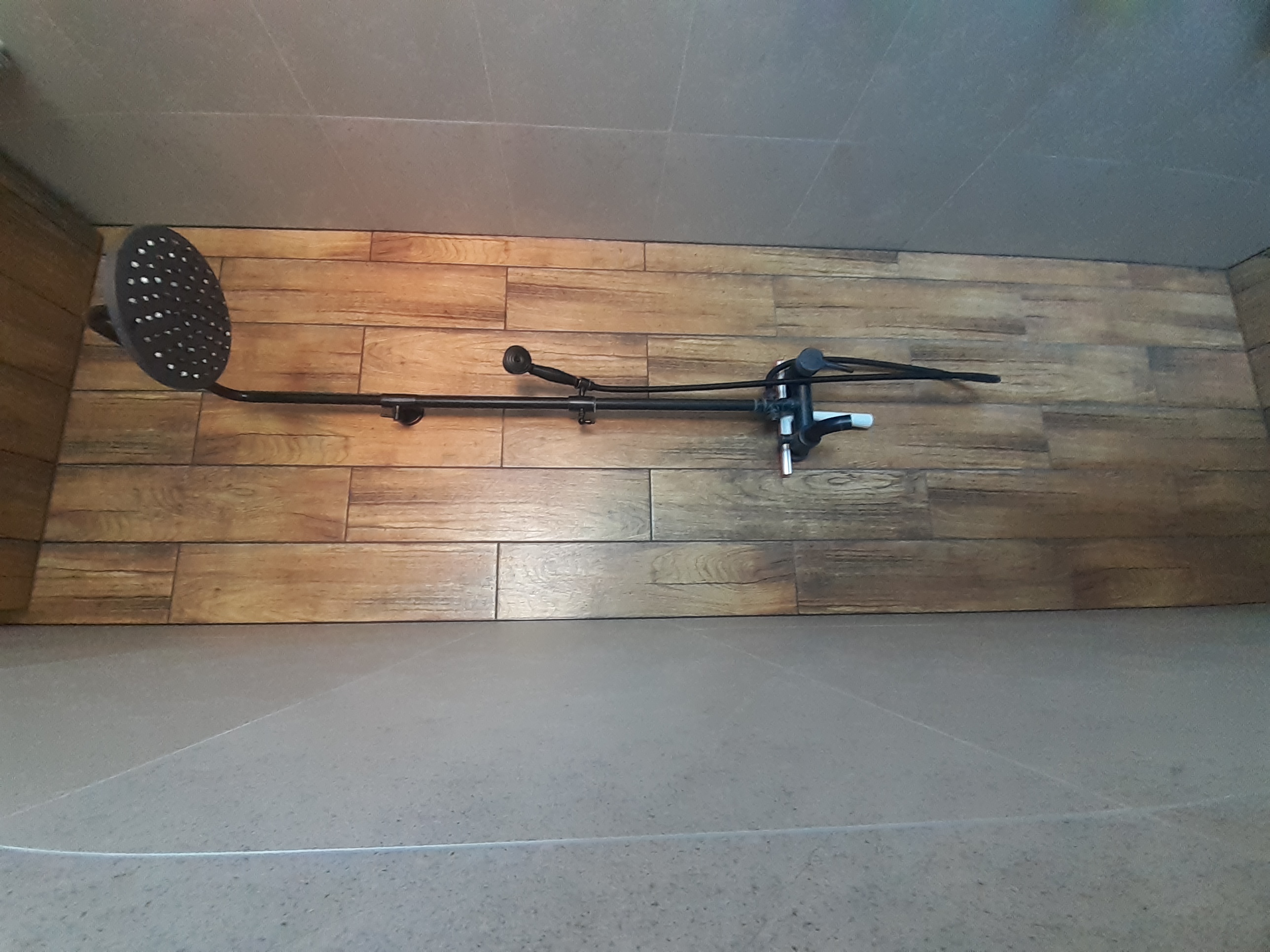 Czarny zestaw natryskowy z deszczownicą i baterią termostatyczną zamontowany na ścianie wyłożonej panelami imitującymi drewno w wyremontowanej łazience.