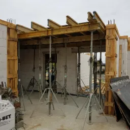 Budowa domu z białych bloczków: widok na szalunek stropu podpartego stalowymi stemplami, z widocznymi zbrojeniami i stosem bloczków Hydro-Bet.