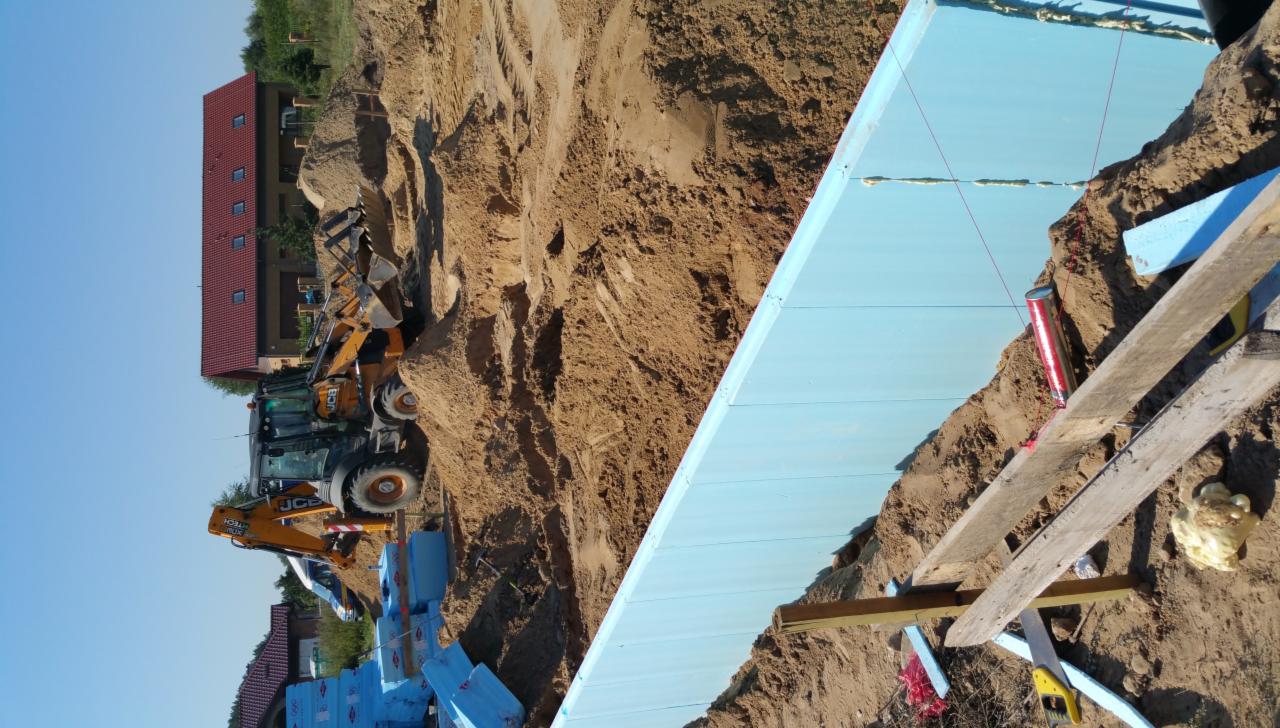 Przygotowanie podłoża pod fundamenty z użyciem niebieskich płyt izolacyjnych i koparki JCB w tle.