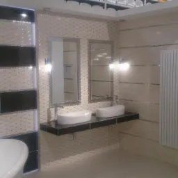 Nowoczesna łazienka z wanną, dwoma umywalkami nablatowymi na czarnym blacie, lustrami z oświetleniem, grzejnikiem drabinkowym i wykończeniem ścian w beżowo-czarnej mozaice.