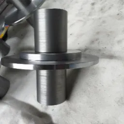 Surowe elementy metalowe, prawdopodobnie po obróbce, ułożone na brudnej powierzchni, widoczne ślady po obróbce skrawaniem.