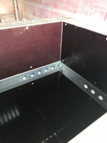 Szczegółowe ujęcie szalunku z płyty wiórowej z metalowymi wzmocnieniami, widoczne otwory montażowe i surowy stan wykończenia.