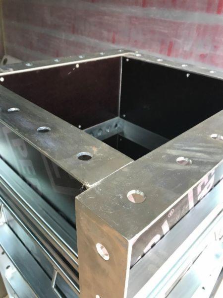 Szczegółowe ujęcie szalunku z metalowymi elementami z otworami, tworzącego kwadratową konstrukcję z widocznym wnętrzem wyłożonym ciemną płytą.